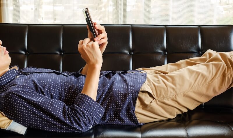 ソファでスマートフォンを操作する男性